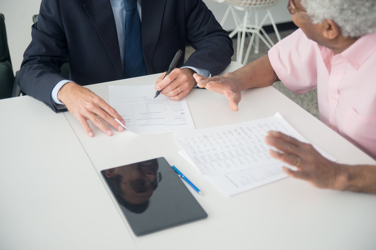 services-10 A business meeting between an elderly client and a consultant discussing documents at an office table.
